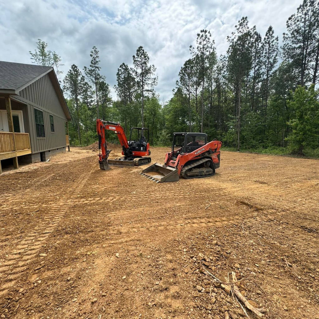 Skid Steer and Mini Excavator in cleared field next to a house.