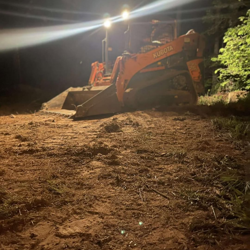 Orange skid steer at night in cleared and leveled yard.